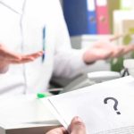 Doctor Fined BIG For Refusing THIS! Doctor gesturing during consultation with patient holding paper with question mark