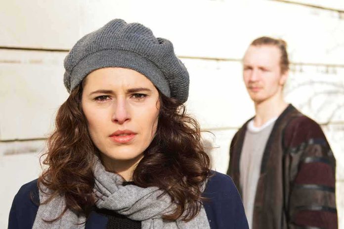 shutterstock_1011733618 woman in gray beret and scarf with man blurred in background