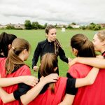 RECALL: 122,000 Cases Of Sports Drink — Is Your KID Drinking It? Coach talks to youth team in a huddle on a field