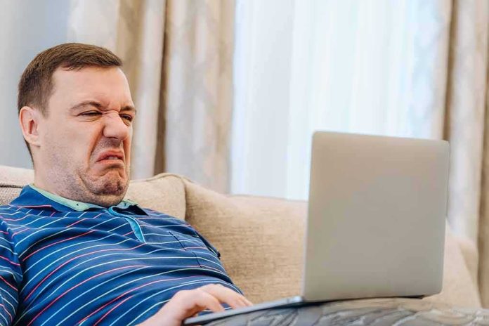 shutterstock_2121979469-1 Man grimacing while using a laptop on a couch