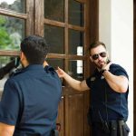 Deadly Warrant Arrest – What TRAGEDY Officers Found Inside Two police officers check a wooden door with glass panels