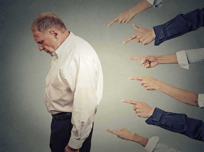 shutterstock_269714324 Man looking down while multiple hands point at him
