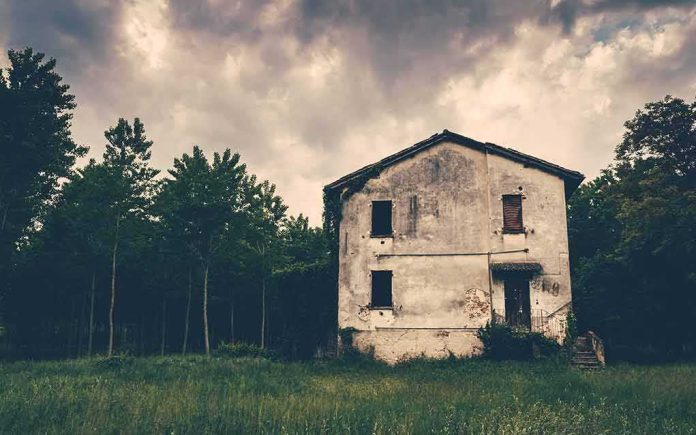 abandoned house in a field under stormy sky