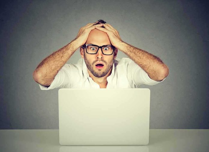shutterstock_637883344 Man with glasses looking shocked at laptop